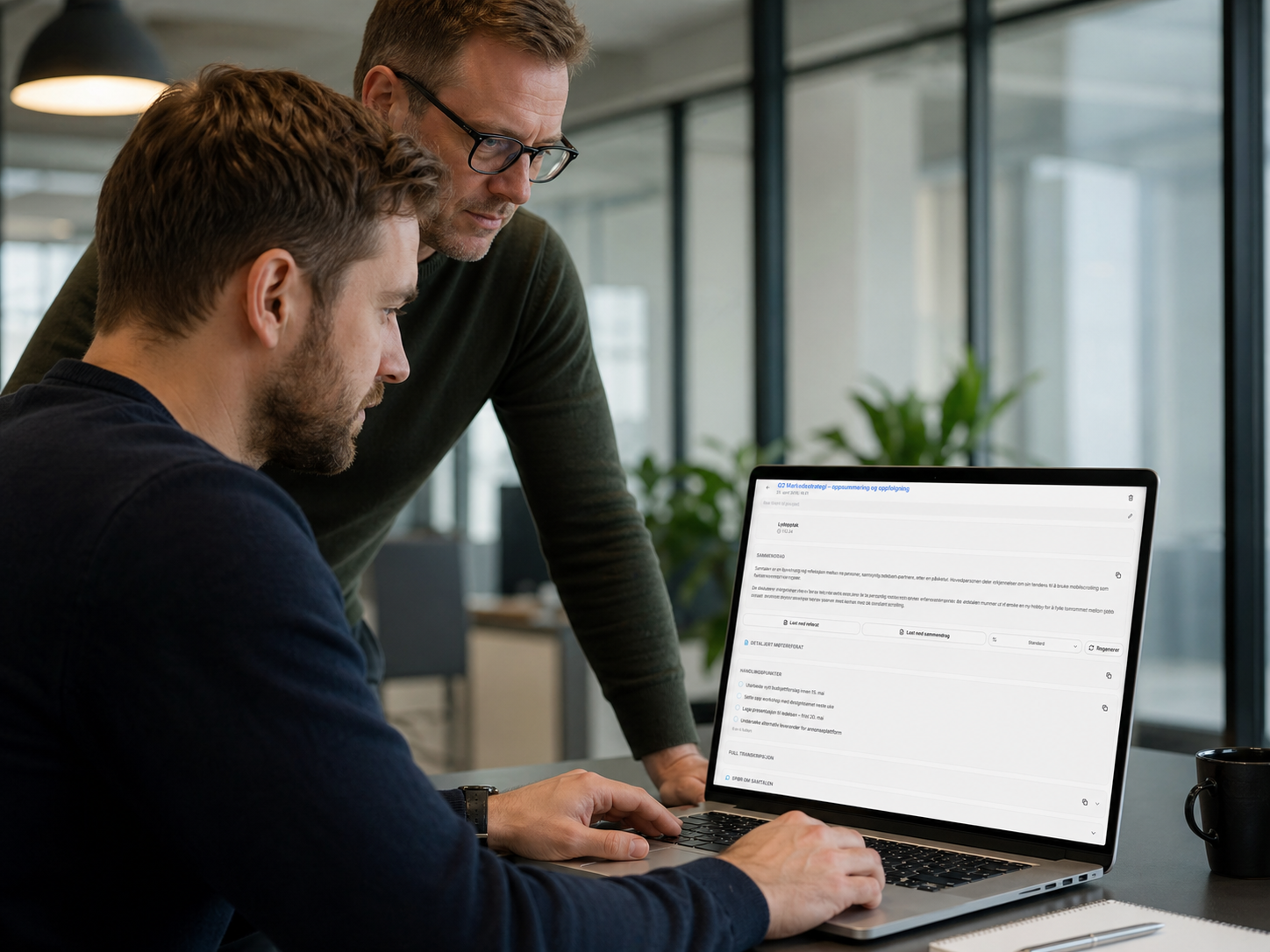 To kollegaer som ser på et automatisk møtereferat på en bærbar PC